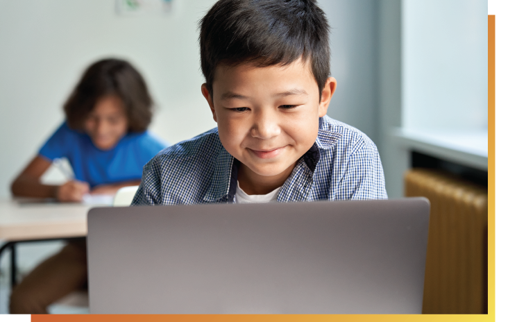 smiling young boy sitting in front of laptop looking down