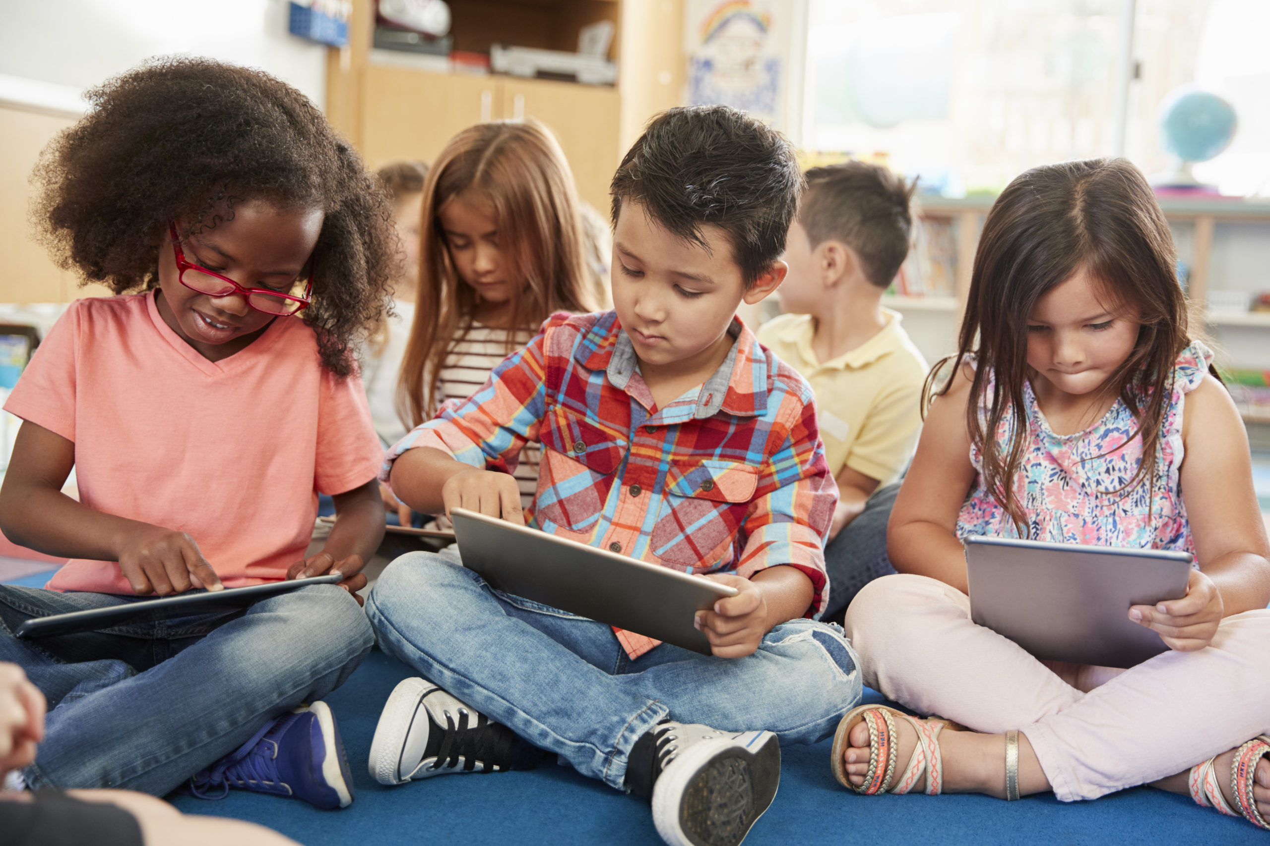 young students sitting crosslegged holding tablets in their laps.