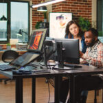 Two engineers sitting at a desk in front of computers showing interest in the implications for AI in education.