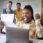 Female university student smiling and cheering in front of her computer after receiving the results from an online formative assessment tool.